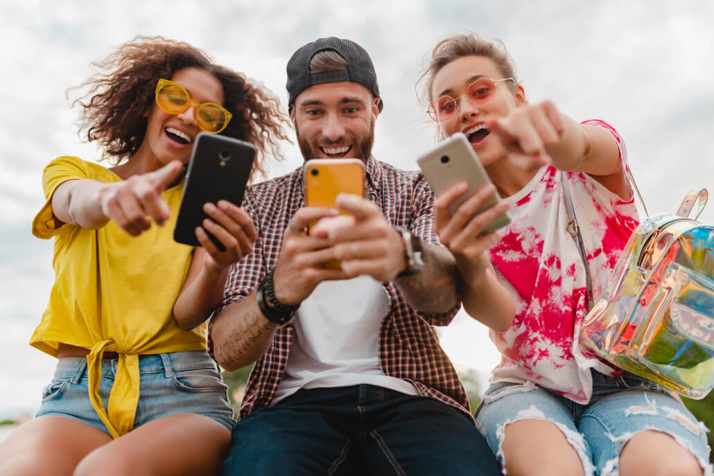 happy-young-company-smiling-friends-sitting-park-using-smartphones 2 (1)