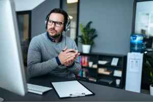 Professional translator with headset conducting video conference at desk with documents and computer monitor.