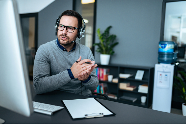 Professional translator with headset conducting video conference at desk with documents and computer monitor.